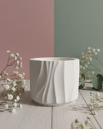 A white Jesmonite candle in a Modern Wave Vessel, presented on a wooden surface with delicate white flowers.