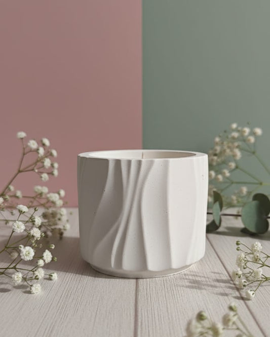 A white Jesmonite candle in a Modern Wave Vessel, presented on a wooden surface with delicate white flowers.