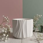 A white Jesmonite candle in a Modern Wave Vessel, presented on a wooden surface with delicate white flowers.