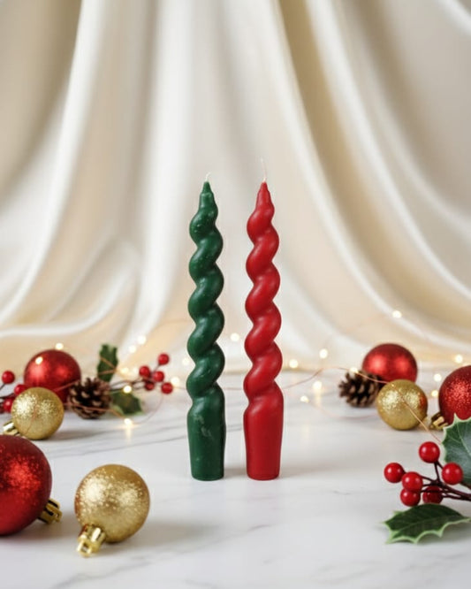 Front view of a set of two Christmas twisted taper soy wax candles, one red and one green, with festive decorations.