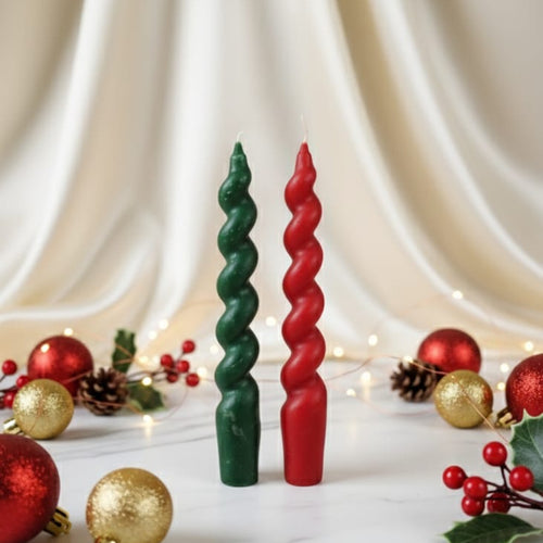 Front view of a set of two Christmas twisted taper soy wax candles, one red and one green, with festive decorations.