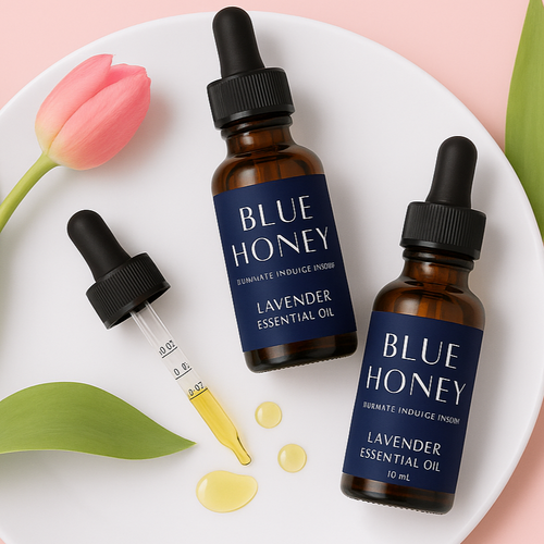 Blue Honey Lavender Essential Oil bottles and dropper with oil droplets on a white plate, styled with a pink tulip and green leaf.