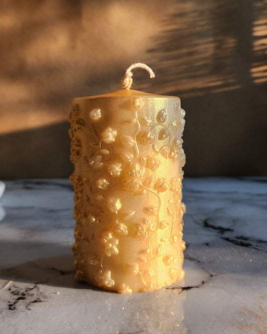 gold dust flower pillar candle with cotton wick on a white marble table top.