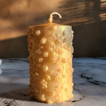 A 4-inch tall gold dust soy wax pillar candle with intricate floral embossing, perfect for gifts.