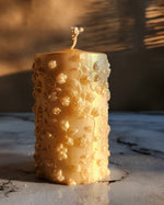 A 4-inch tall gold dust soy wax pillar candle with embossed floral details.