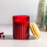 A ruby glow scented ribbed cylindrical glass jar candle with its lid resting beside it.