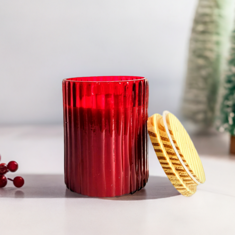 A ruby glow scented ribbed cylindrical glass jar candle with its lid resting beside it.