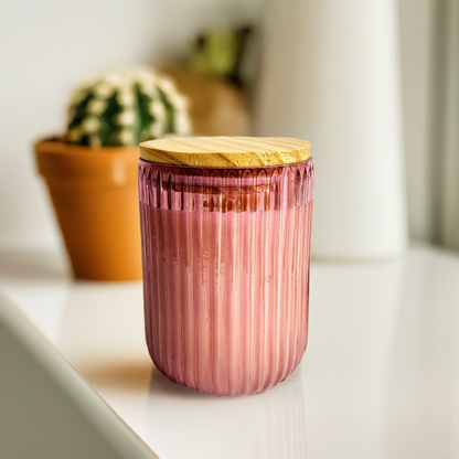 Pink ribbed U-shaped glass jar candle with wooden lid.