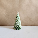 A green Christmas tree-shaped soy wax pillar candle with intricate detailing, presented from a front view.