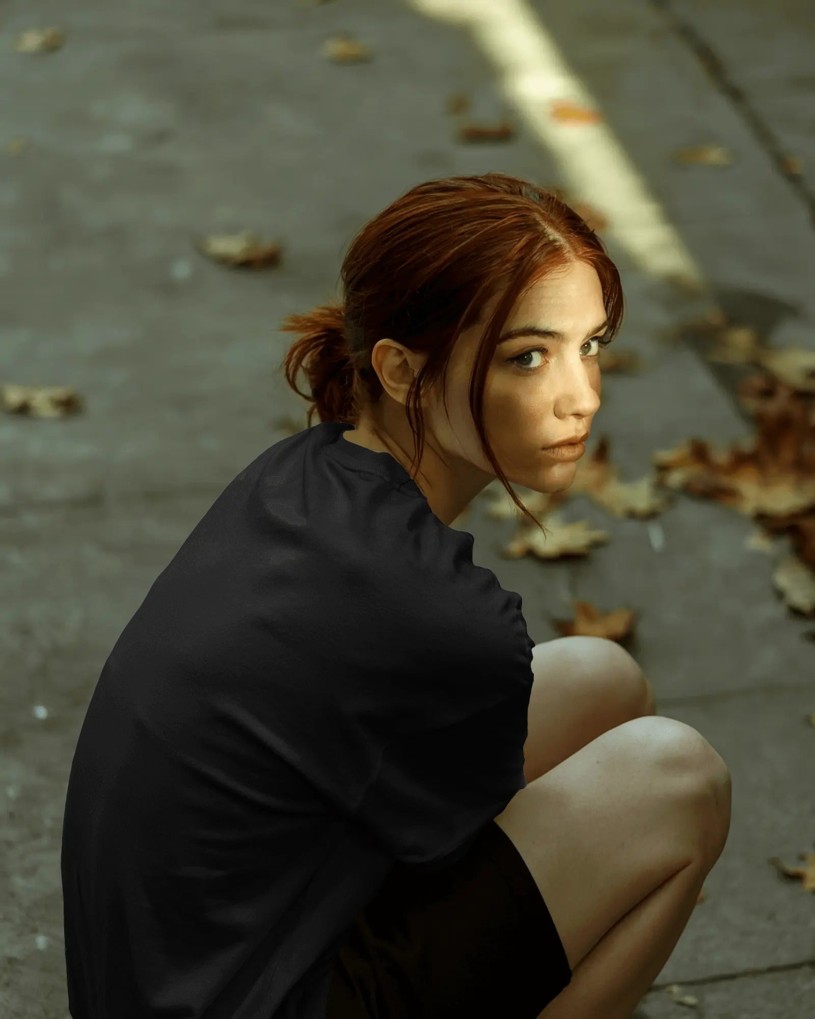 a white female model sitting down on the side of a road wearing an oversized Thalassophile tshirt