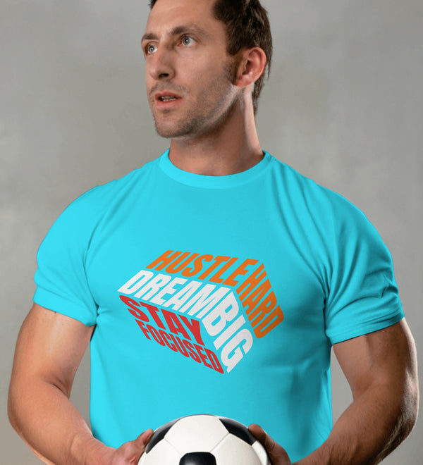 Cyan t-shirt with 'Hustle Hard Dream Big Stay Focused' graphic, worn by a man holding a soccer ball.