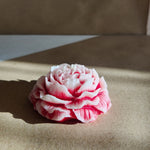 A pink and white peony flower-shaped soy wax candle with a rose scent, displayed from the front.