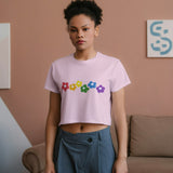 Front view of a young woman wearing a pink Rainbow Bloom crop top with colorful flowers and grey pants.