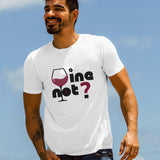 A man wearing a white "Wine Not?" graphic t-shirt, smiling outdoors against a blue sky.