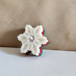 A festive snowflake-shaped candle with red, green, and white layers, perfect for Christmas decor.