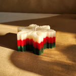 A festive snowflake-shaped pillar candle with red, green, and white layers, perfect for Christmas decor.