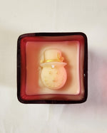 Top view of a red glass jar candle featuring a white snowman with a gold hat and glitter details.