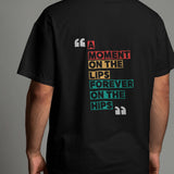 Back view of a black oversized t-shirt with colorful modern typography that reads 'A Moment on the Lips, Forever on the Hips'.