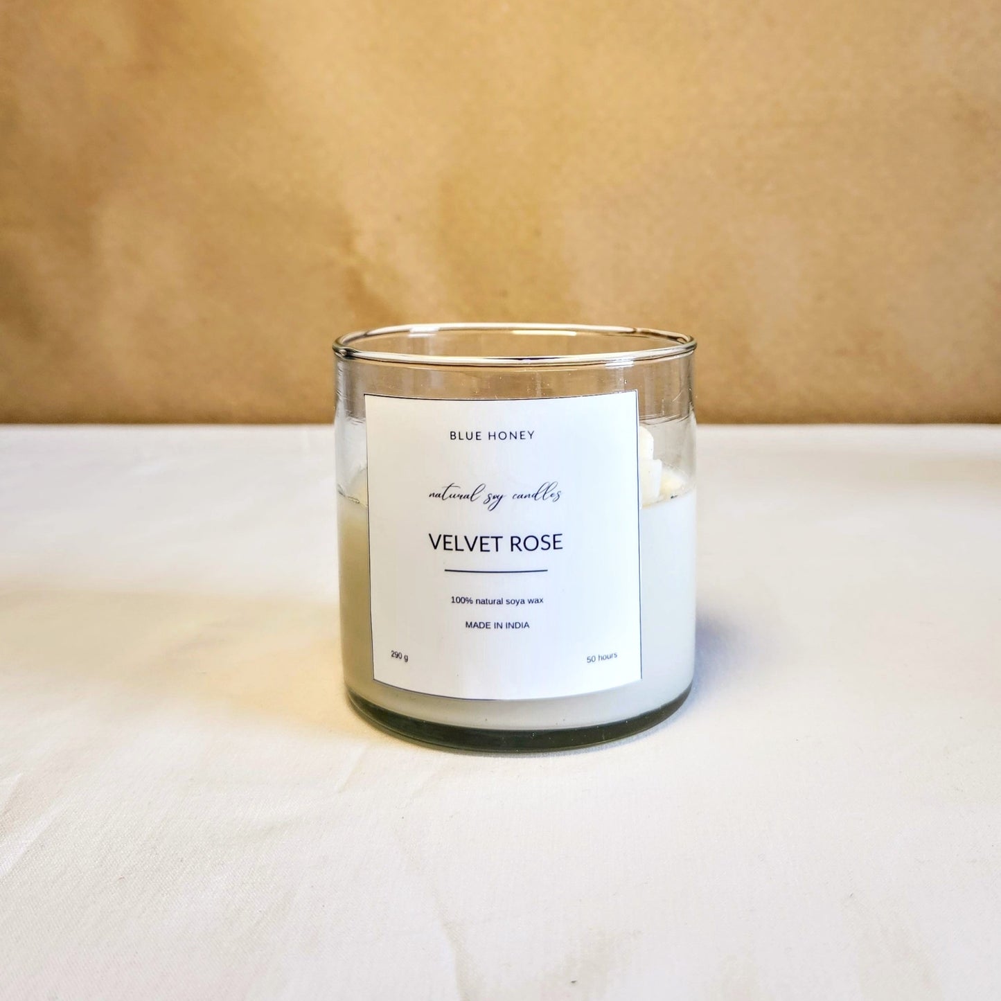 daisy flower candle inside a clear jar on a table top. label reads Velvet Rose