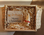 Close-up detail of a Christmas gnome candle in a gift box with shredded paper and a Merry Christmas card.
