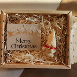 Close-up detail of a Christmas gnome candle in a gift box with shredded paper and a Merry Christmas card.